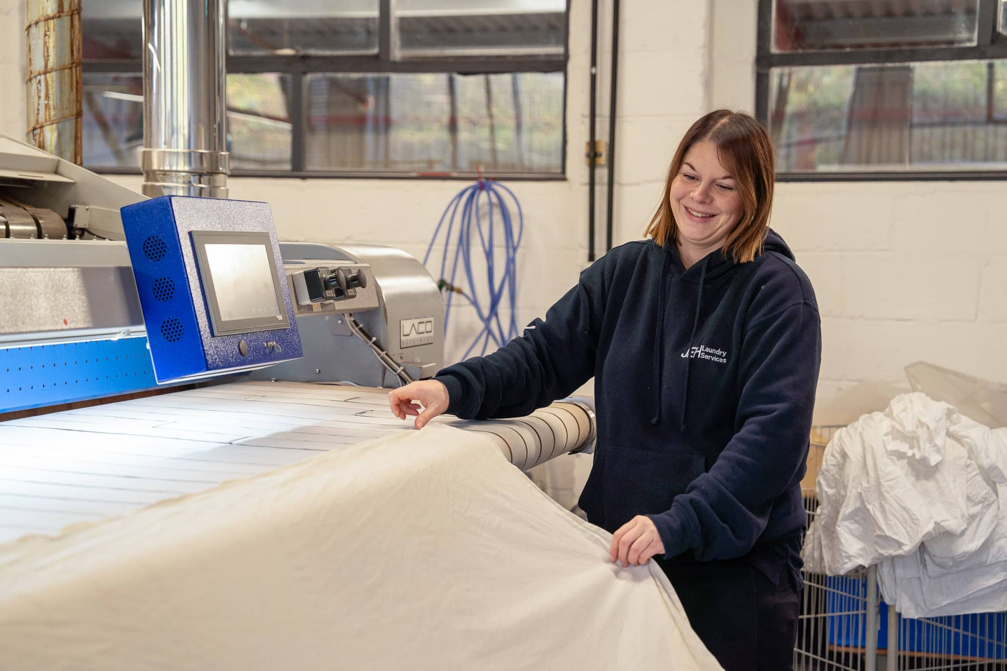 JEH Laundry Services staff member working on the ironing press